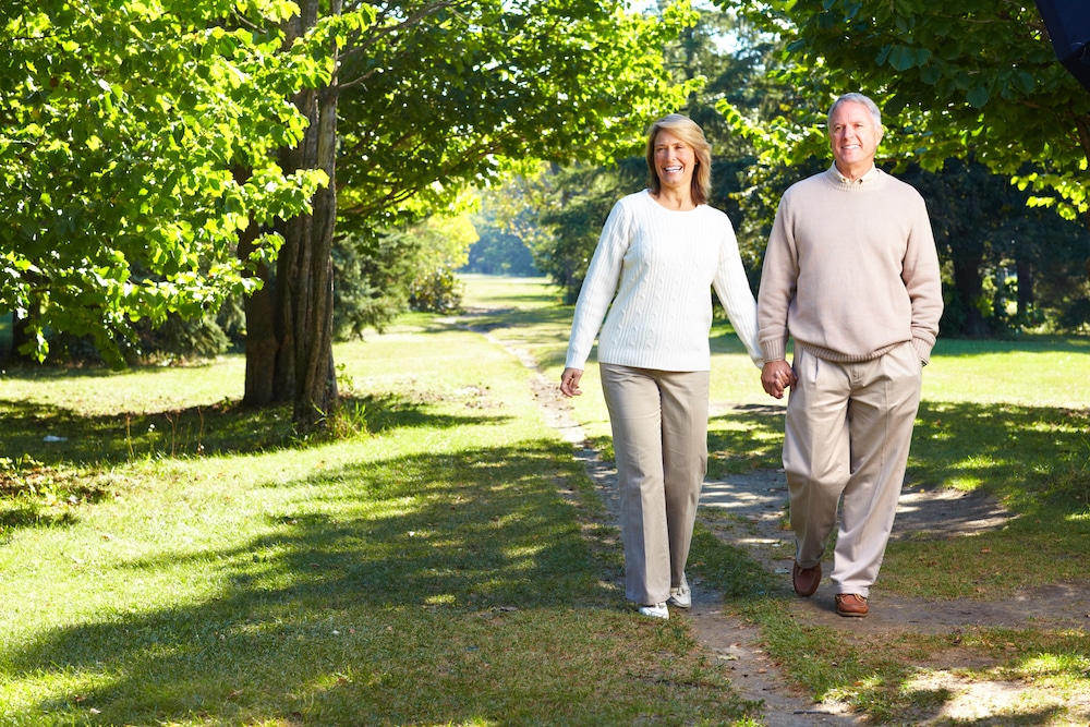 A smiling senior couple holds hands as they walk through a park