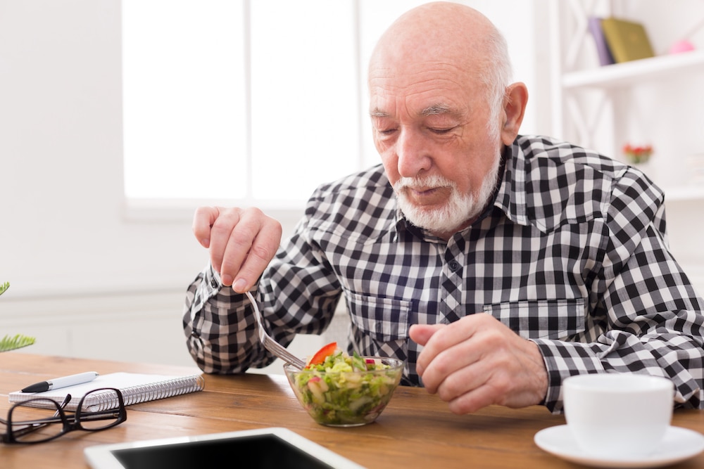 A senior man eating a healthy salad while sitting at a table